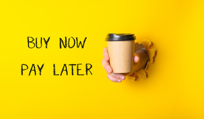 A person is holding a coffee cup with the words Buy Now Pay Later written on the wall behind them