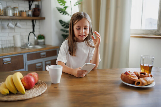 Preteen girl having video call on smartphone near breakfast at home - Powered by Adobe