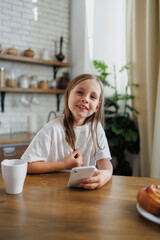 Portrait of smiling kid holding smartphone near breakfast at home