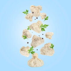 Fototapeta premium Delicious khinkali (Georgian dumplings), peppercorns and parsley falling on light blue background