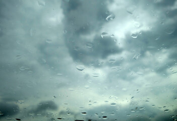 Cloudy sky seen from car window with rain drops on it.