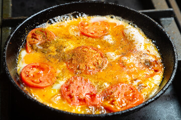 Eggs with tomatoes and onions in a pan are fried in oil.