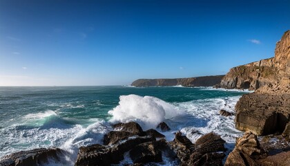 Waves crashing onto a rocky shoreline with dramatic cliffs and a clear blue sky in the background.