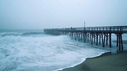 Obraz premium A misty pier extending into turbulent waves under a cloudy sky.