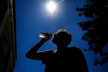 Young attractive man drinking cold water in sunny day. Surviving the heat concept 