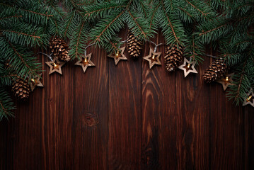 Christmas background with fir branches, cones and star shape lights on dark wooden board. Top view. Copy space. Xmas decoration