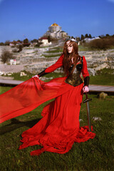 Beautiful red haired girl in metal medieval armor dress with sword standing in warlike pose