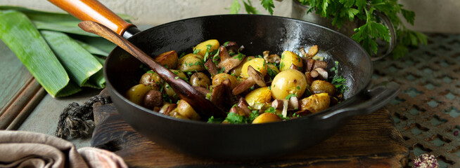 frying pan with fried new potatoes with boletus mushrooms on the table