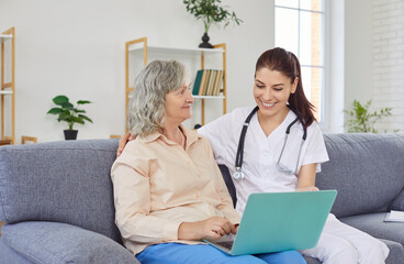 Supporting caring kind female medical nurse helping senior patient with laptop online, assisted...
