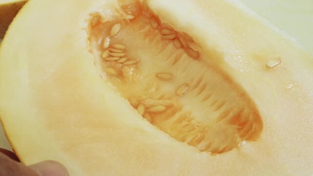 Seeds are scooped out of a melon cut lengthwise. Medium shot.
