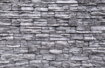 Weathered panels of gray stone coating wall made of striped stacked slabs of natural rocks. Background and texture.