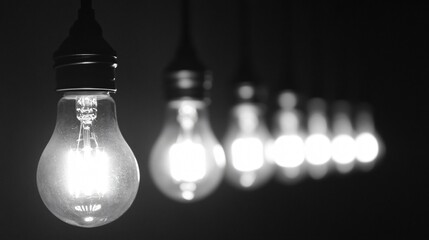 A black and white photograph of a row of light bulbs hanging from the ceiling, each bulb emitting a different level of brightness, creating a gradient effect