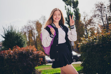 Photo of adorable friendly girl dressed bomber walking college showing v-sign outdoors urban city park