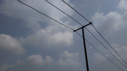 Fototapeta premium An upward view of power lines stretching across a cloudy sky. The image captures the simplicity of infrastructure against a natural backdrop, making it ideal for themes of connectivity or energy.