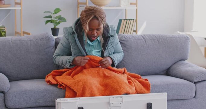 Afro American female at home, frozen in freezing cooled flat in warm coat, blanket shivering tremble with cold, unhappy lady feels bad suffer of heating system problem, climate, temperature regulation