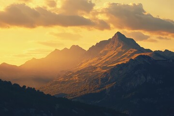Obraz premium Majestic mountain peaks bathed in warm sunset light, with dramatic clouds and forested slopes in the foreground