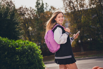 Photo of pretty dreamy girl dressed bomber short skirt backpack communicating modern device outdoors urban city park