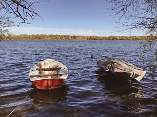 Two boats are floating in a lake, one of which is covered with a tarp. The scene is peaceful and...