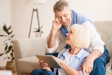 Happy elderly couple searching film on digital tablet, resting at home on weekends
