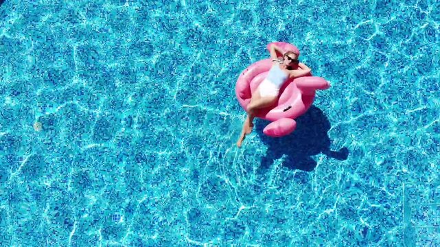 Aerial drone view of woman on pool flamingo float in pool in hotel. Summer holidays, enjoying summer vacations. Aerial drone view
