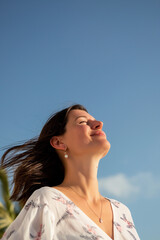 Happy woman enjoying summer sunshine and fresh air on holiday, hair blowing in breeze