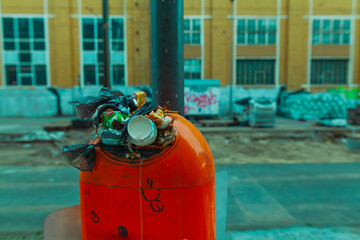 An overfilled trash can with a lot of garbage sticking out of the opening, city cleanliness, urban...