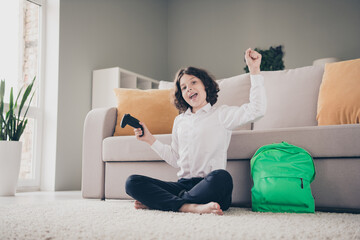 Photo of excited crazy cheerful boy schoolkid sitting carpet winning playstation home apartment room interior indoors
