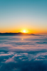 Obraz premium Golden sun rising behind mountains, illuminating a dreamy sea of clouds