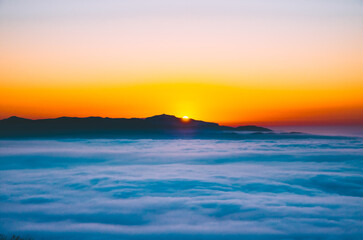 Golden sun rising behind mountains, illuminating a dreamy sea of clouds