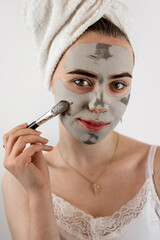 Pretty woman applying with brush clay or mud facial mask isolated on white