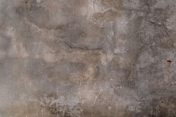 A grey wall with cracks and holes. The wall is rough and uneven, giving it a worn and aged appearance