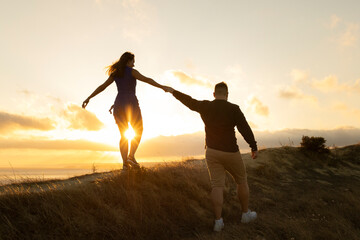 Fototapeta premium Loving couple walking on a hill at sunset holding hands