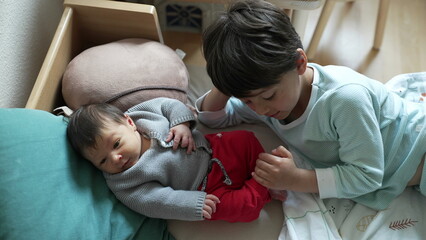 Obraz premium Older sibling lies beside a newborn baby, sharing an affectionate and tender moment, highlighting the loving bond and connection in a cozy home setting