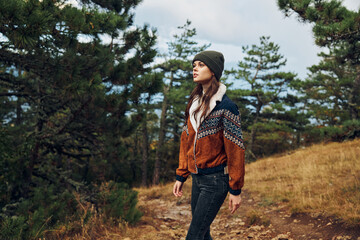 A woman in a stylish hat and jacket taking a leisurely stroll along a serene forest trail, surrounded by tall pine trees