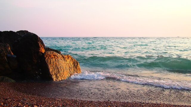 Waves gently lap at shore during stunning sunset over ocean. Golden sunlight reflects off waves as they roll onto shore, creating tranquil atmosphere at sunset by sea. Montenegro summer Canj