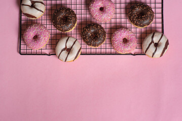 Assorted donuts on cooling rack with pink background, variety of toppings.