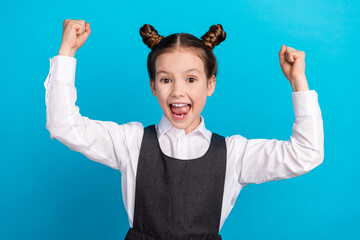 Photo portrait of cute little girl raise fists winning dressed stylish school uniform isolated on blue color background