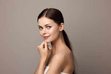 Beautiful young woman posing with hand on chin, looking at camera, closeup on gray background