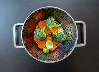 Collapsible food steaming basket in a pot with broccoli, carrots and Brussels sprouts vegetables. Steaming helps retain the essential nutrients and flavour and helps in controlling the calorie intake.
