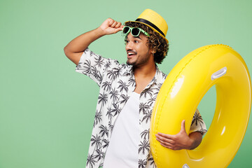 Young shocked Indian man he wears beach shirt hat rest near hotel pool hold rubber ring take off...