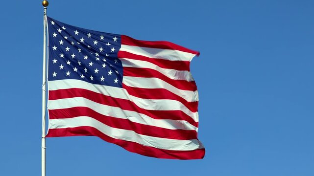 Real American flag waving in the wind in slow motion, with vibrant red white and blue colors against blue sky, 4k, with copy space.