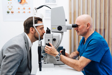 Attractive male doctor ophthalmologist is checking the eye vision of handsome middle age man in...