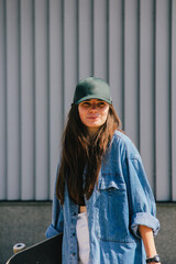 A young woman in a green cap and denim jacket, captured in a candid moment with a skateboard. The graininess and blur add a gritty, urban artistic effect to the photograph.
