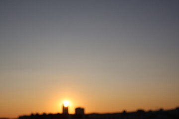 A sunset over the city, with delicate shades of orange and bluish, as the sun dips below the horizon. Clouds create serenity and drama to the scene.