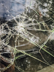 Shattered car window, displaying intricate patterns of cracked glass, vertical close-up. Perfect for illustrating accident damage, vehicle destruction and the fragility of glass in automotive contexts