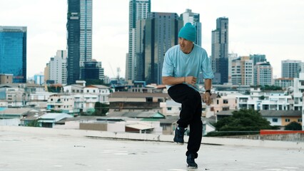 Skilled caucasian B-boy dancer practicing street dancing at rooftop with city sites or urban. Motion shot of young man performing street dance by doing freeze pose. Outdoor sport 2024. Hiphop.