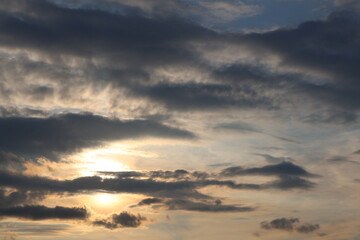 A sunset over the horizon, with delicate shades of gold and grey, as the sun dips below the horizon. Clouds create serenity and drama to the scene.