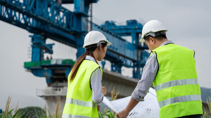 Two construction workers wearing safety gear standing in front of a large blue crane.