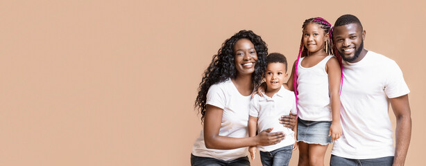 Happy millennial family. Portrait of smiling african parents with their two little kids over yellow background