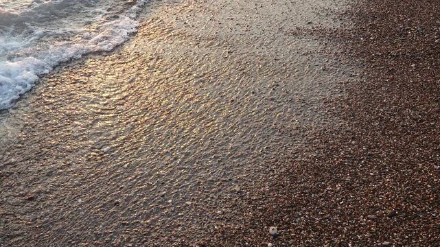 Waves gently lap at shore during stunning sunset over ocean. Golden sunlight reflects off waves as they roll onto shore, creating tranquil atmosphere at sunset by sea. Montenegro summer Canj